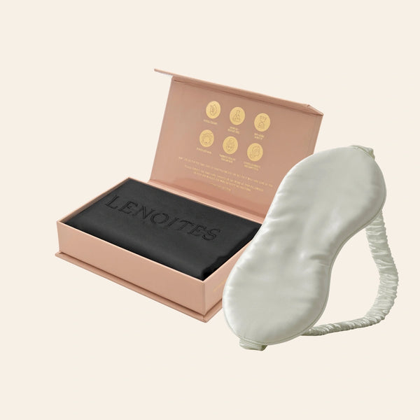 Pillowcase and Sleep Mask in Mulberry Silk by Lenoites featuring a grey silk sleep mask and a black mulberry silk pillowcase presented in an open blush pink box against a soft light background.