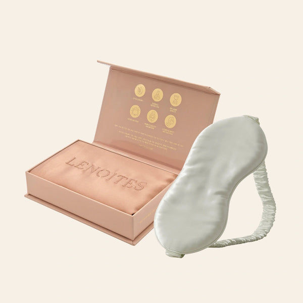 Pillowcase and Sleep Mask in Mulberry Silk by Lenoites featuring a grey silk sleep mask and a rosegold mulberry silk pillowcase presented in an open blush pink box against a soft light background.