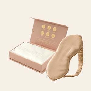 Pillowcase and Sleep Mask in Mulberry Silk by Lenoites featuring a beige silk sleep mask and a white mulberry silk pillowcase presented in an open blush pink box against a soft light background.